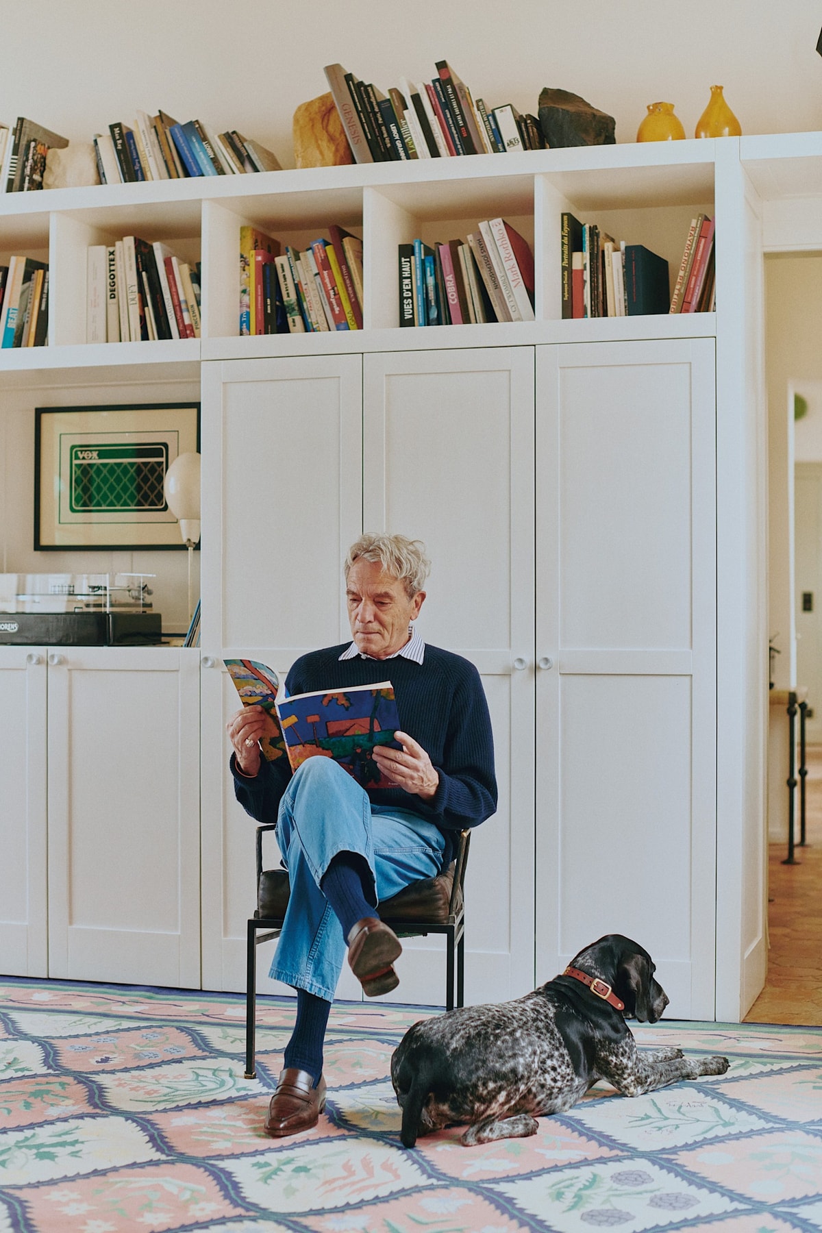 Eric Schmidt reading in a room with built-in bookshelves and a dog in the foreground