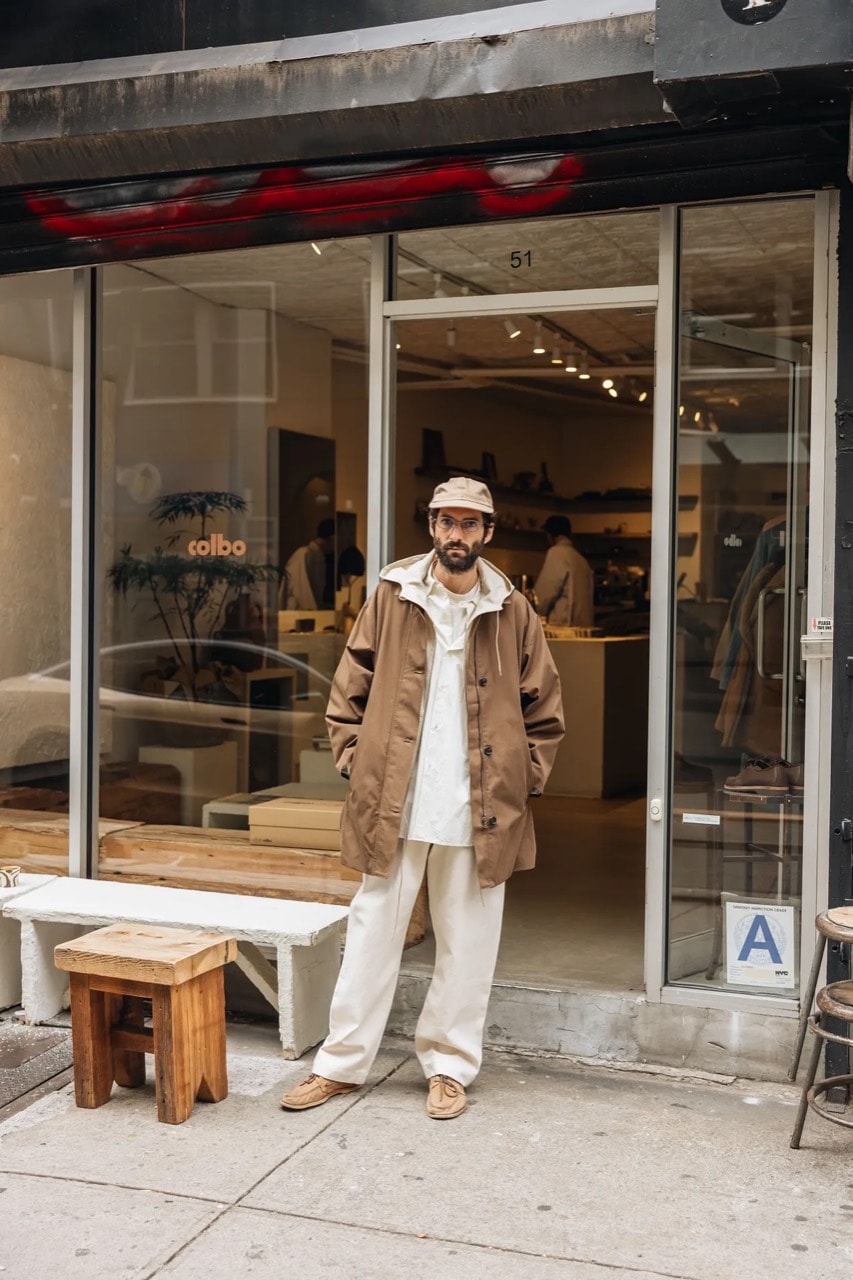 Tal Silberstein standing outside a storefront wearing a brown coat, white shirt, cream trousers, and tan shoes